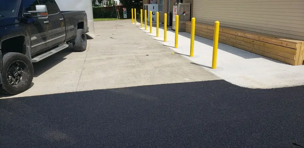 Finished concrete walkway and apron with bollards beside new asphalt