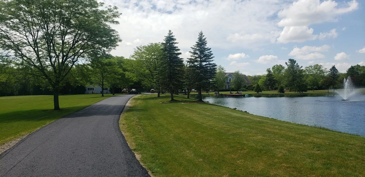 Finished asphalt lane winding past a pond to a country home