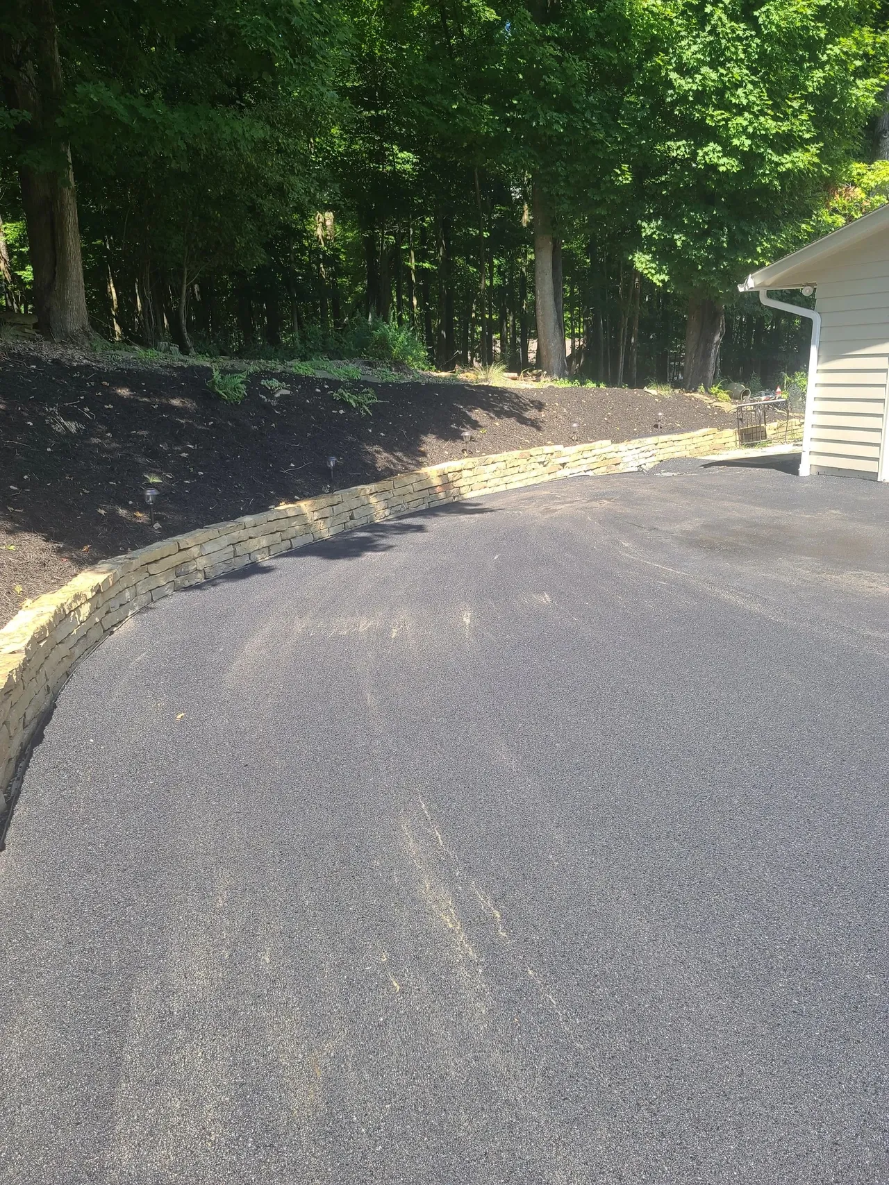 Stone-lined asphalt driveway on a wooded lot