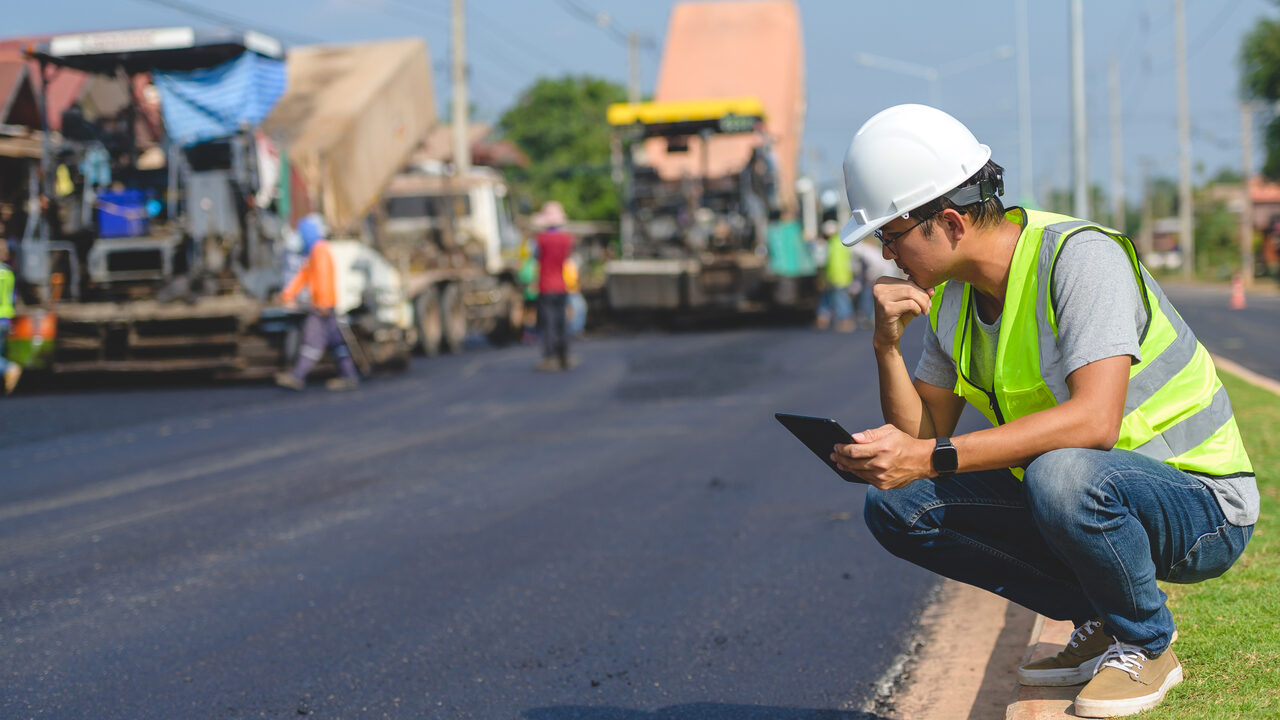 A site supervisor checking plans beside a freshly paved road