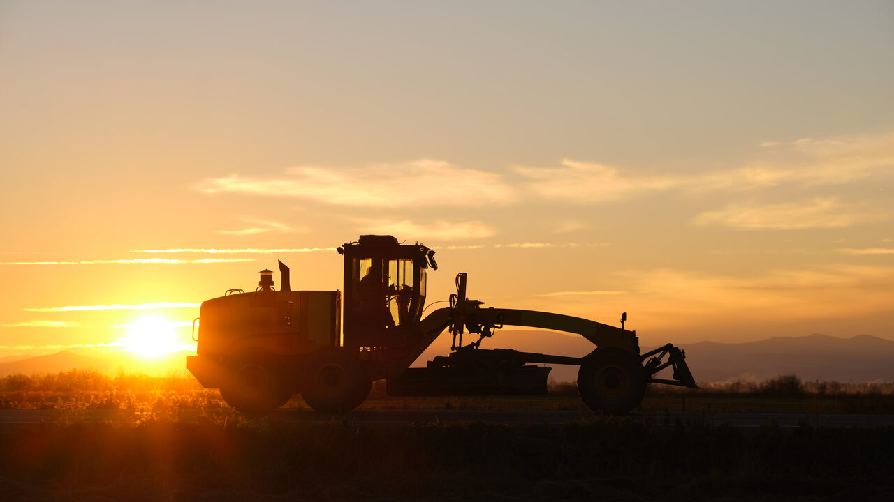 A motor grader silhouetted against the sunset on a grading site