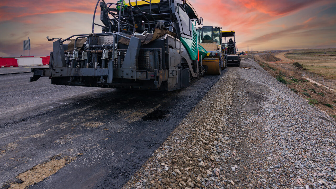 An asphalt paver laying a new road surface at sunset